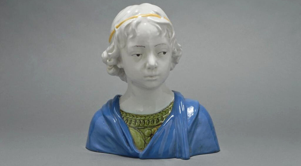 Ceramic majolica bust of a young boy wearing a green tunic and blue robe